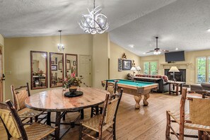 Un espace repas avec une table et des chaises en bois, un billard, et un salon avec un canapé et une cheminée.