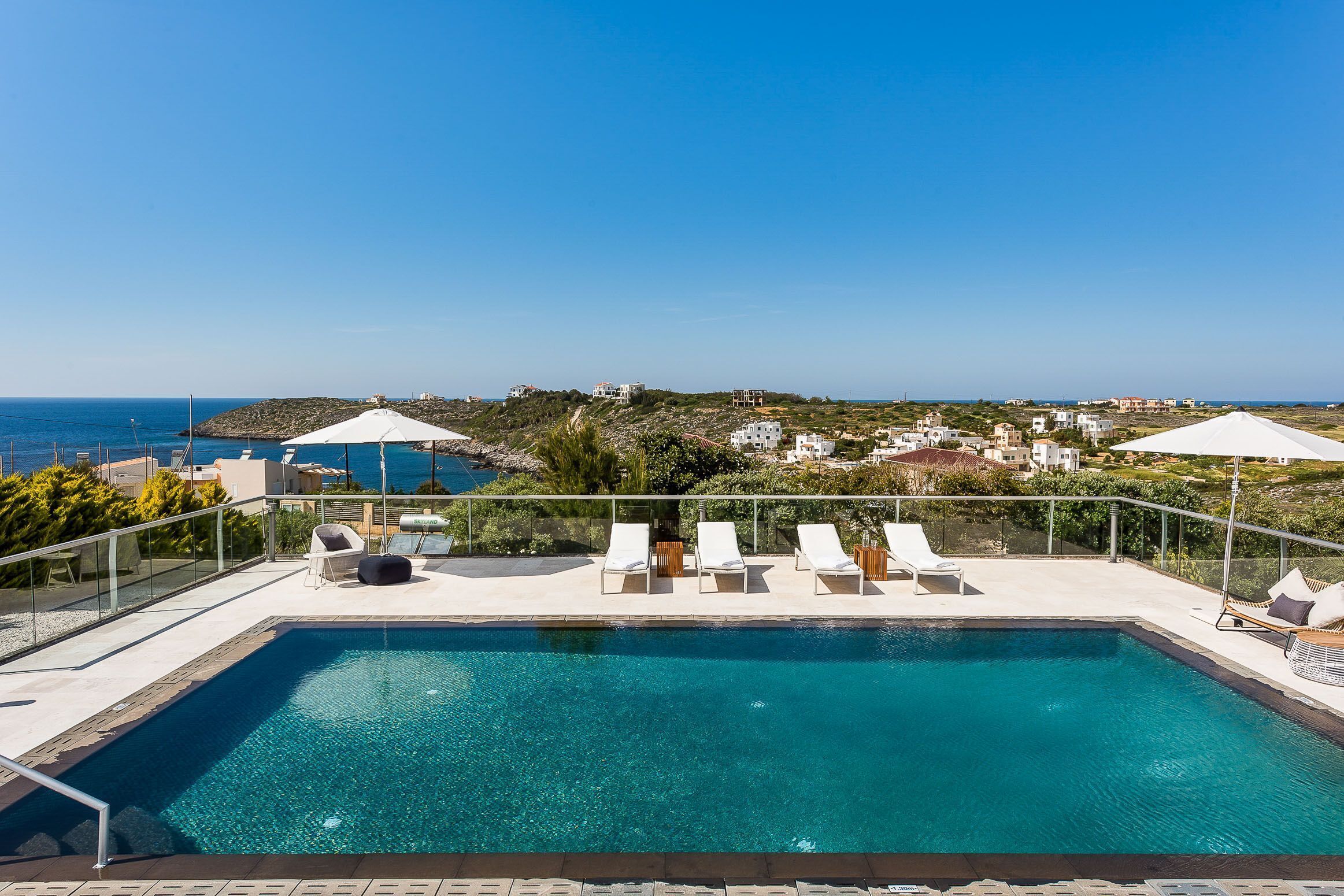 A swimming pool with lounge chairs and umbrellas, overlooking a coastal landscape with buildings.