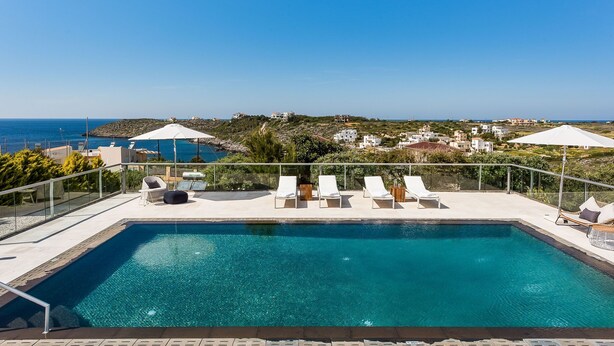 Una piscina con sillones de descanso y sombrillas, con vistas a un paisaje costero con edificios.