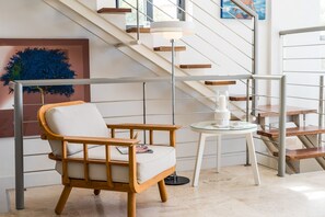 A modern interior with a wooden chair, a small round table, and a staircase with metal railings.