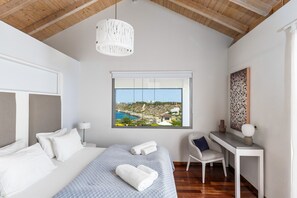 A bedroom with a bed, a desk, a chair, a window with a view, and a hanging light fixture.