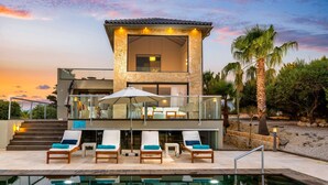 Un edificio moderno de dos pisos con área de piscina, asientos al aire libre y vista al atardecer.