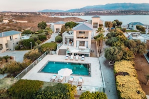 A modern resort with a pool, lounge chairs, and a view of the sea.