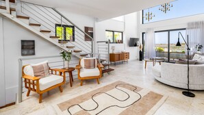 Ein großzügiger Wohnbereich mit Treppe, einer Sofagarnitur, einem Couchtisch und Blick ins Freie.