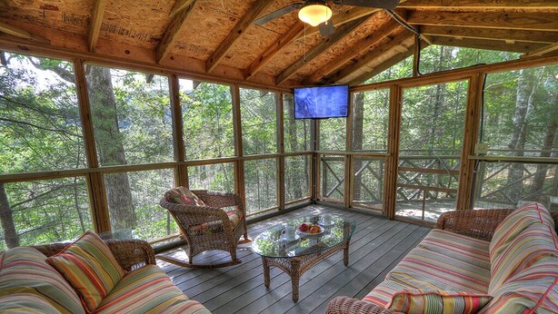 Terraza de madera con mobiliario de mimbre y una mesa de vidrio, con vistas a un bosque.