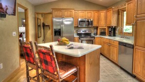 Una cocina con armarios de madera, un refrigerador, un microondas, una estufa y un lavavajillas. Hay una zona de comedor con una mesa y sillas.