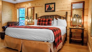 A wooden cabin bedroom with a large bed, a chair, a nightstand, and a mirror.