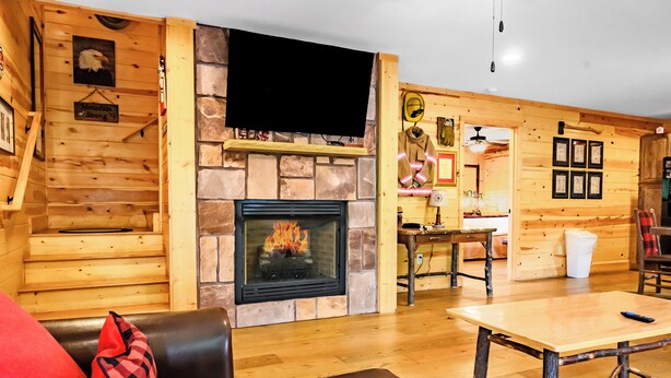 A cozy cabin interior with a fireplace, wooden walls, a leather sofa, and a dining area.