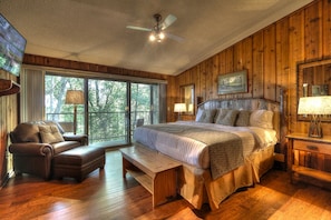 A spacious bedroom with a large bed, a leather sofa, a wooden bench, and a ceiling fan.