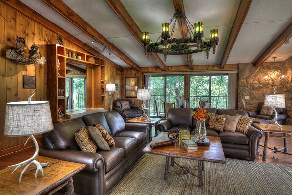 A cozy living room with leather sofas, a chandelier, and a stone wall.