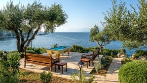 A pool table set on a stone patio with benches, overlooking a body of water. - Villa Aliki - Five Bedroom Villa, Sleeps 10 (Kassiopi)
