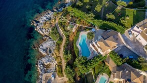 An aerial view of a coastal property with multiple buildings, a swimming pool, and a rocky shoreline. - Villa Aliki - Five Bedroom Villa, Sleeps 10 (Kassiopi)