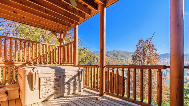 A wooden deck with a stone fireplace, wooden railing, and a view of mountains and trees.