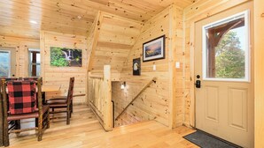 A wooden cabin interior with a dining area, a staircase, and a door leading outside.