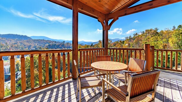 A wooden deck with a round table and chairs, overlooking a mountainous landscape. - Big Sky: Mountain-Side Cabin Surrounded by Majestic Views Only 2 Miles from Gatlinburg (Gatlinburg)