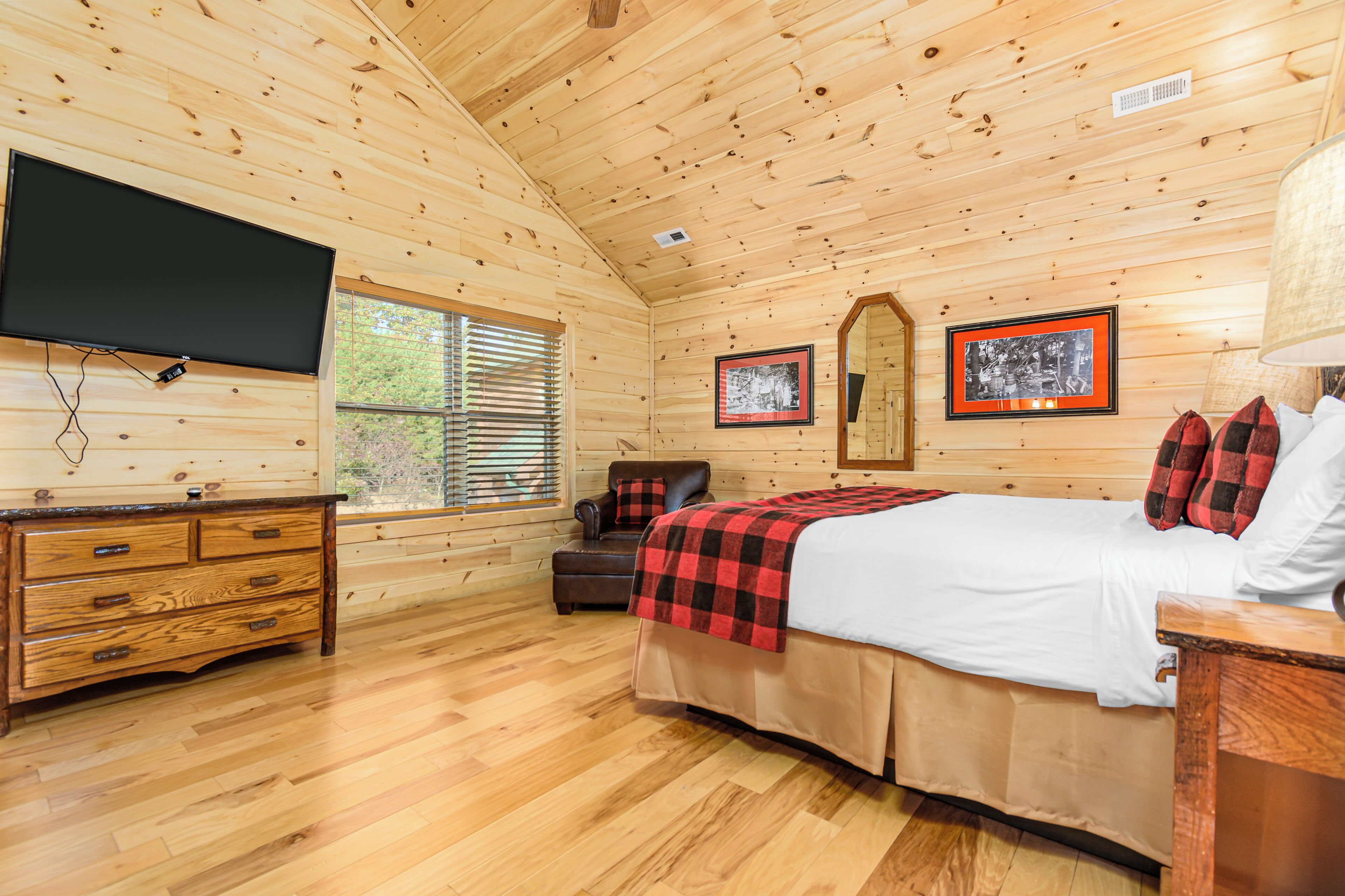 Ein Schlafzimmer einer Holzhütte mit Bett, Kommode, Fernseher und gerahmten Bildern an der Wand.