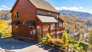 A wooden log cabin with a balcony, surrounded by autumn foliage and a mountainous backdrop. - Big Sky: Mountain-Side Cabin Surrounded by Majestic Views Only 2 Miles from Gatlinburg (Gatlinburg)