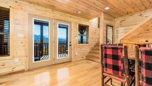 A wooden cabin interior with a dining area, two doors leading to a balcony, and a view of the mountains. - Big Sky: Mountain-Side Cabin Surrounded by Majestic Views Only 2 Miles from Gatlinburg (Gatlinburg)