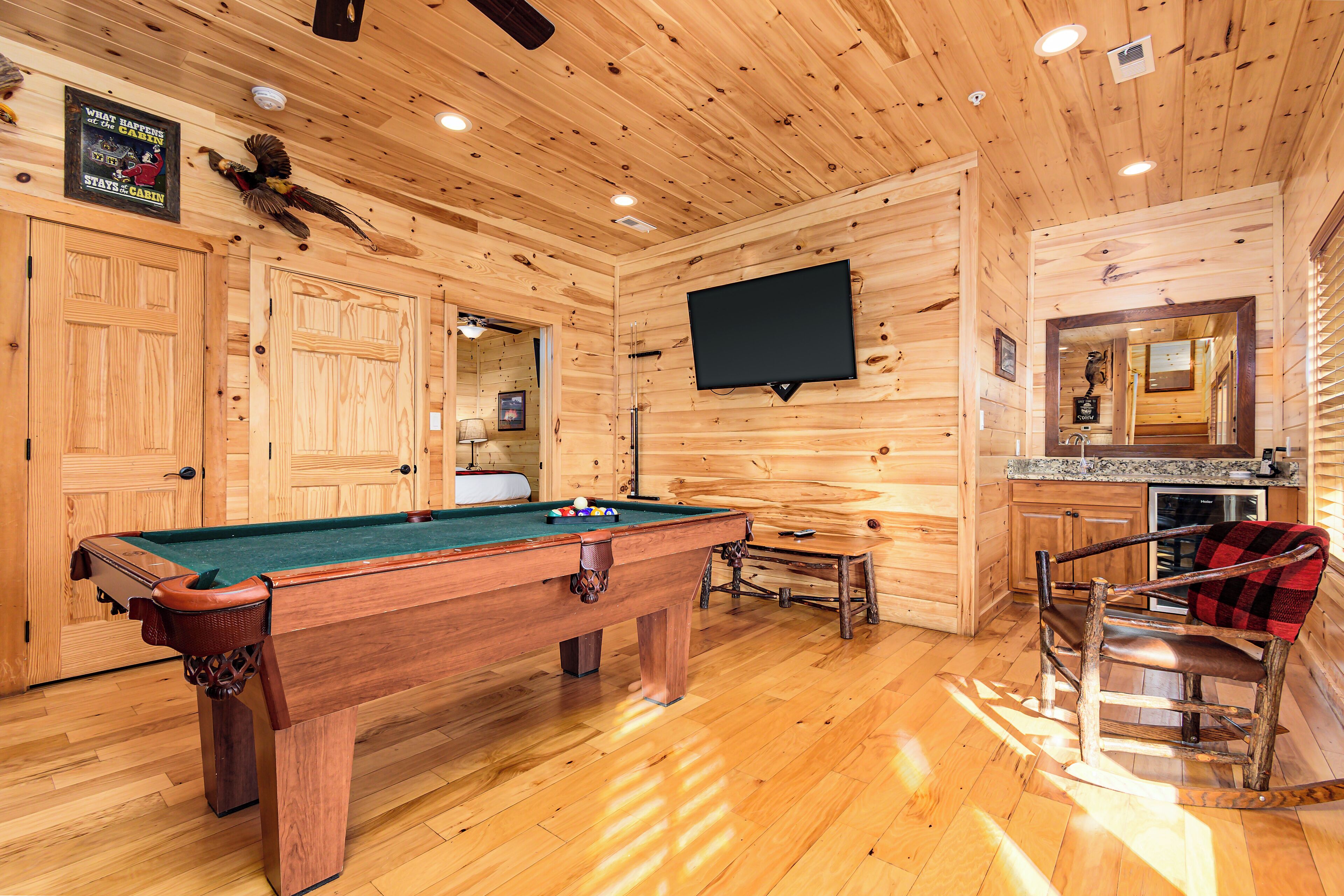 A wooden cabin interior with a pool table, a television mounted on the wall, and a cozy seating area with a fireplace.