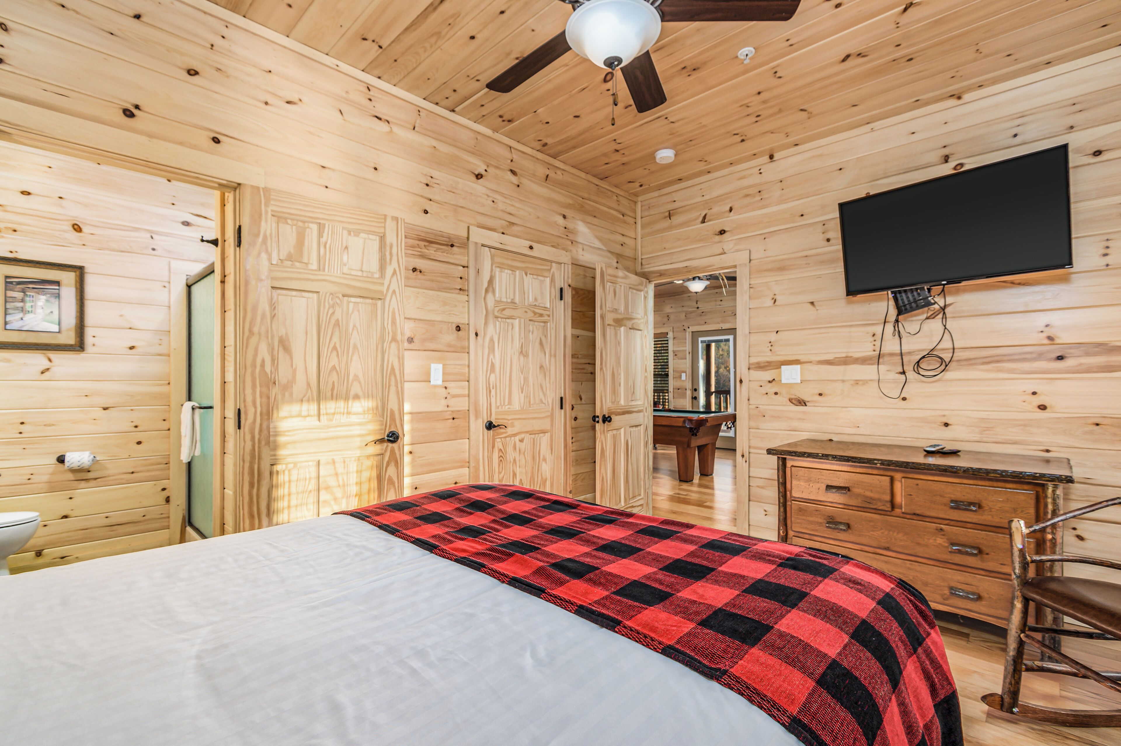 Une chambre dans un chalet en bois, comprenant un lit, une commode, un téléviseur et un ventilateur de plafond.