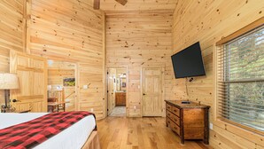 A wooden cabin room with a bed, dresser, TV, and a window with blinds. - Big Sky: Mountain-Side Cabin Surrounded by Majestic Views Only 2 Miles from Gatlinburg (Gatlinburg)