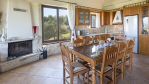 A spacious kitchen with a large dining table, wooden cabinets, and a fireplace.