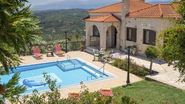 A stone villa with a swimming pool, outdoor seating, and a view of the mountains.
