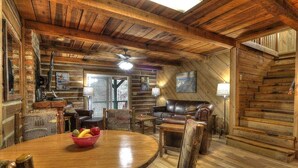 Interior rústico de cabana com mesa de jantar de madeira, sofá de couro e escada.
