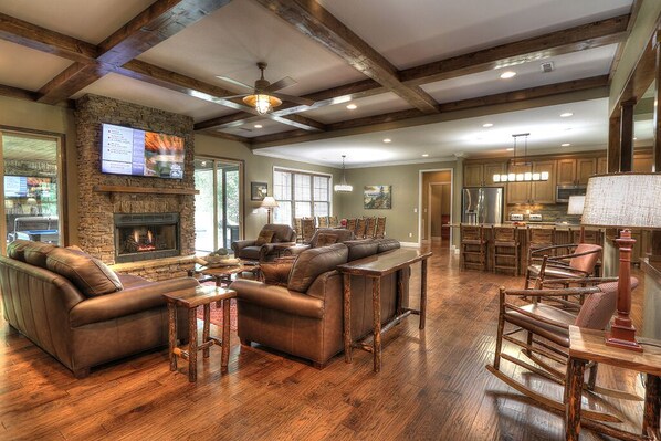 A spacious living room with a fireplace, leather sofas, wooden flooring, and a kitchen area with wooden cabinets and a bar.
