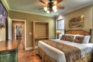 A bedroom with a wooden headboard, a bed with patterned bedding, a ceiling fan, and a painting on the wall.