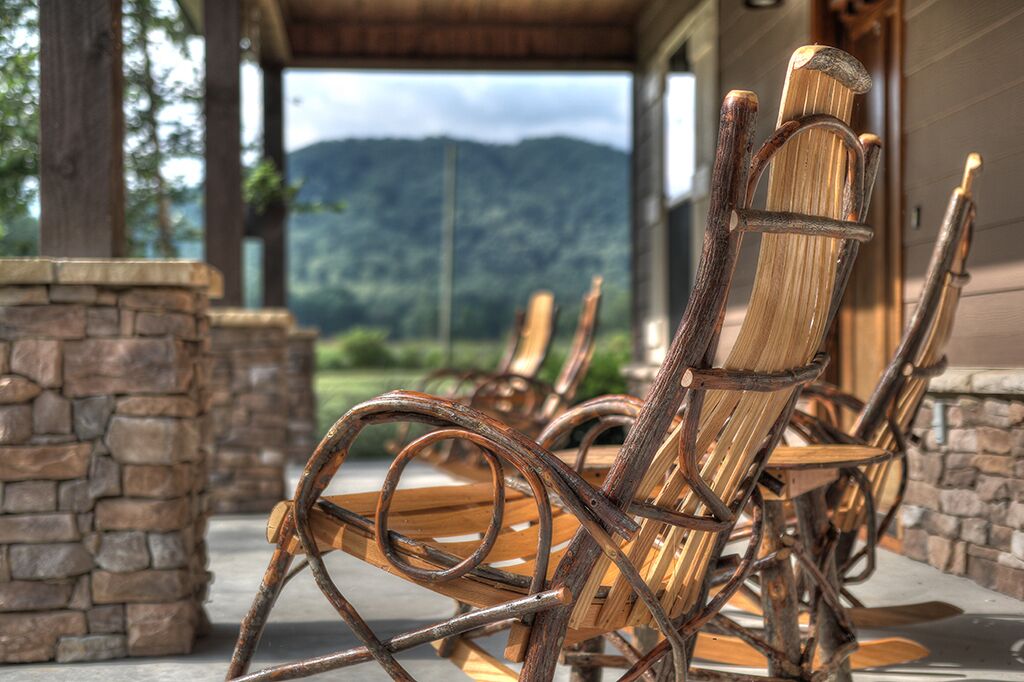 Outdoor wooden chairs with metal frames, stone walls, and a view of mountains.