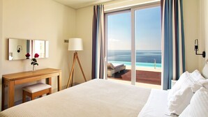 Habitación de hotel con una cama grande, un escritorio, una silla, una lámpara y vistas al océano a través de una puerta corrediza de vidrio.
