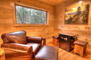 Interior de una cabaña de madera con un sofá de cuero, una mesita de madera y un cuadro de un paisaje forestal.