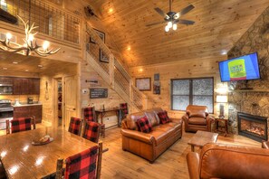 Ein gemütliches Blockhaus-Interieur mit Essbereich, Ledersofa, Kamin und einem an der Wand montierten Fernseher.