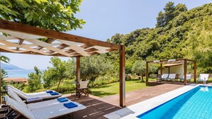 Eine Holzterrasse mit Pool, Liegestühlen und einer Pergola.