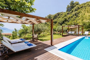 A wooden deck with a pool, lounge chairs, and a pergola. - Villa Apollo - Four Bedroom Villa, Sleeps 8 (Pelekas)
