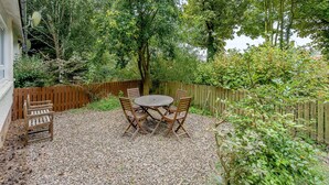 A patio with a round table and four chairs, surrounded by gravel and greenery. - Burnside West Cottage- UK39596 (St Andrews)