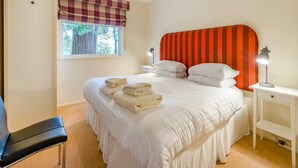 A neatly made bed with white linens and folded towels, a bedside table with a lamp, a window with plaid curtains, and a chair. - Burnside West Cottage- UK39596 (St Andrews)