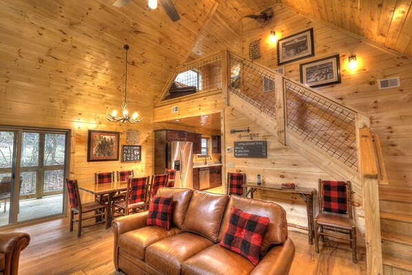 A wooden cabin interior with a dining area, a sofa, and a staircase.