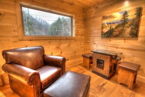 A log cabin interior with a leather armchair, ottoman, and a wooden cabinet with a radio.