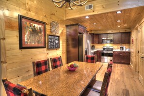 A wooden interior with a dining table, chairs, and a kitchen area with appliances.