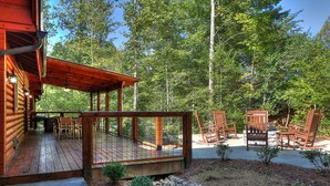 A wooden cabin with a deck, outdoor seating, and a forest backdrop.