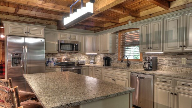 A modern kitchen with granite countertops, stainless steel appliances, and wooden ceiling beams.