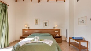 A bedroom with a wooden headboard, a green bedspread, two bedside tables with lamps, and artwork on the walls.