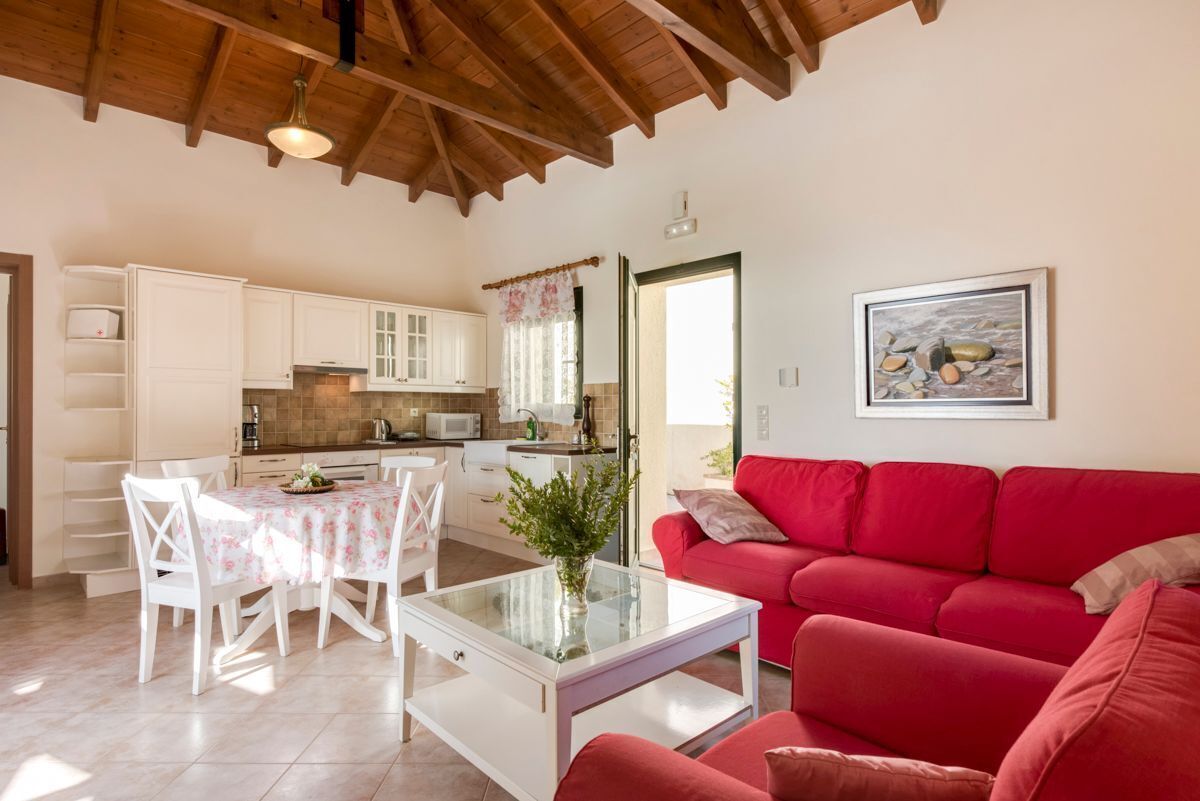 A spacious living area with a red sofa, a dining table with chairs, and a kitchen in the background.