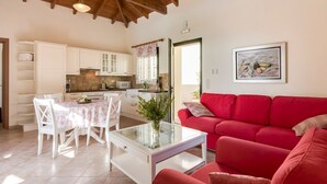 A spacious living area with a red sofa, a dining table with chairs, and a kitchen in the background.
