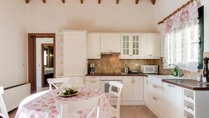 A kitchen with white cabinets, a round table with a floral tablecloth, and a window with a floral curtain.