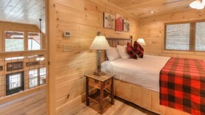 Una habitación de cabaña de madera con una cama, una mesita de noche, una lámpara y una ventana con persianas.