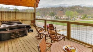 Una terraza de madera con un jacuzzi, mobiliario exterior y vistas a un pueblo.
