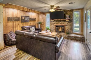 A cozy living room with a leather sofa, a fireplace, and wooden walls.